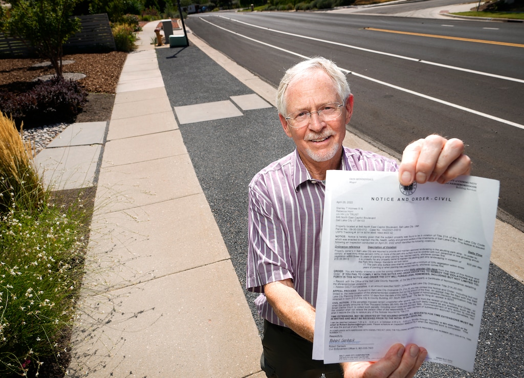 (Leah Hogsten | The Salt Lake Tribune) Salt Lake City resident Stan Holmes holds a notice from Salt Lake City that says his parking strip is noncompliant with city code, Aug. 25, 2022.