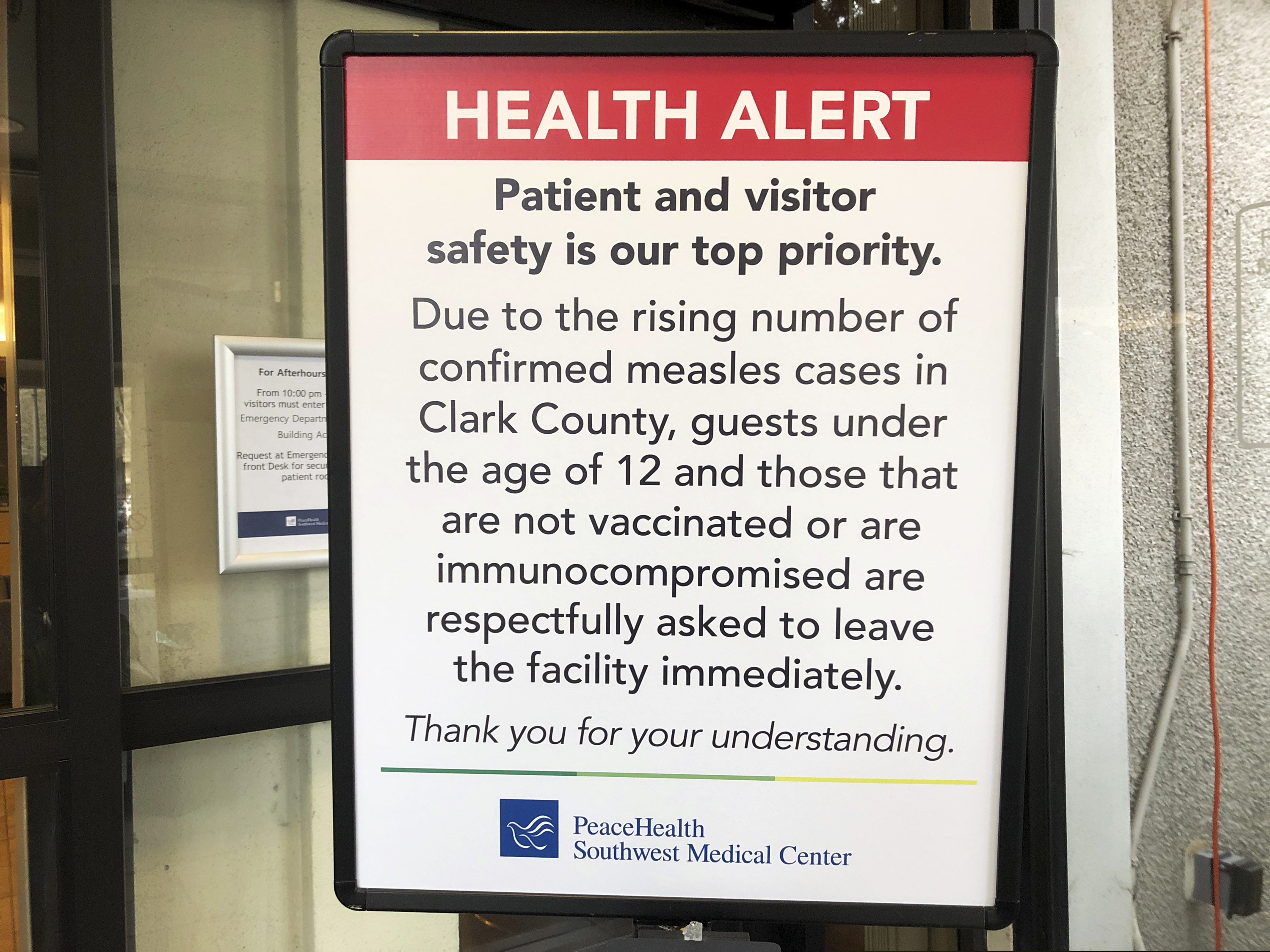 A sign prohibiting all children under 12 and unvaccinated adults stands at the entrance to PeaceHealth Southwest Medical Center in Vancouver, Wash., Friday, Jan. 25, 2019. Washington Gov. Jay Inslee declared a statewide public health emergency Friday as confirmed measles cases rose to 30, with nine more suspected. (AP Photo/Gillian Flaccus)