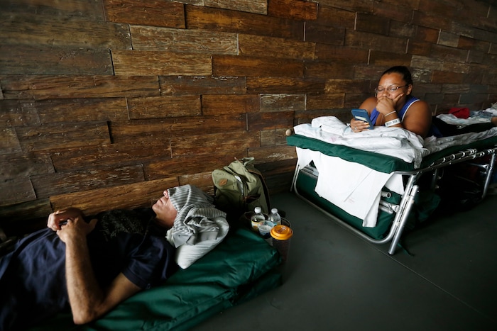 (Wilfredo Lee | AP Photo) This Sept. 14, 2017 file photos shows Margarita Lopez, right, as she looks at her phone as RS Steidle naps at a special needs shelter at Florida International University in Miami, Fla. About 30 people from Key West, Fla., including staff with the Florida Keys Outreach Coalition for the Homeless were sheltered in a storefront underneath a parking garage on campus.