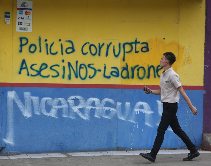 (Alfredo Zuniga | The Associated Press) A man walks past graffiti that reads in Spanish "Corrupt police. Murderers-Thieves," In Managua, Nicaragua, Tuesday, April 24, 2018. Human rights groups say clashes between police and protesters left nearly 30 dead since people took to the streets last week to oppose tax hikes and benefit cuts meant to shore up the ailing social security system.