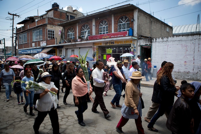In this Aug. 18, 2017 photo, family and friends walk in procession from the church to the cemetery carrying a cross anointed with holy water to mark the grave of murdered doctor and mother Jessica Sevilla Pedraza, 29, in Villa Cuauhtemoc, Mexico state. Many violent crimes such as disappearances often go unreported and unpunished, and the State of Mexico is widely considered ground zero for killings of women in the country today. (AP Photo/Rebecca Blackwell)