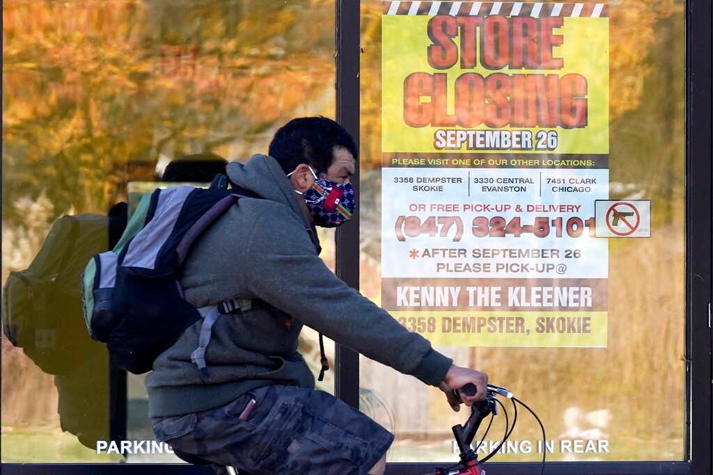 (Nam Y. Huh | AP) A man wearing a face mask rides a bicycle past a closed store in Wilmette, Ill., Friday, Nov. 6, 2020. Illinois reports the biggest spike in unemployment claims of all states.