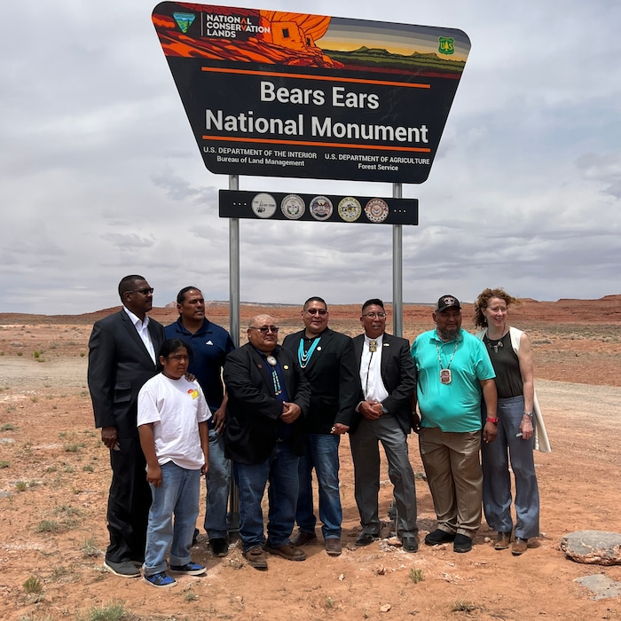 (Photo courtesy of the Bears Ears Inter-Tribal Coalition) Tribal and federal officials met last week at White Mesa, Utah, to sign an historic cooperative agreement for the management of Bears Ears National Monument. Flanked by Undersecretary of Agriculture Homer Wilkes, left, and BLM Director Tracy Stone-Manning, right, members of the Bears Ears Commission gathered at the newly unveiled monument sign on State Road 261. Pictured left to right are Commissioners Christopher Tabbee and son (Ute), Malcolm Lehi (Ute Mountain Ute), Carleton Bowekaty (Zuni Pueblo), Timothy Nuvangyaoma (Hopi) and Davis Filfred (Navajo).