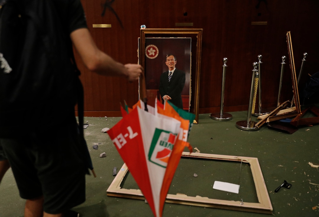 (Vincent Yu | AP Photo) A protester holding an umbrella walks past a damaged chairman picture at the Legislative Chamber after break in to protest against the extradition bill in Hong Kong, Monday, July 1, 2019. The extradition law has aroused concerns that this legislation would undermine the city's independent judicial system as it allows Hong Kong to hand over fugitives to the jurisdictions that the city doesn't currently have an extradition agreement with, including mainland China, where a fair trial might not be guaranteed.