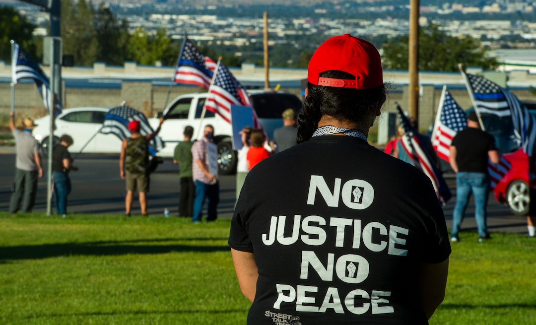 (Rick Egan  |  The Salt Lake Tribune)     Tilesa Fotu watch from a distance as police supporters upset by a Pay Bagley cartoon wave flags, as they protest The Salt Lake Tribune in West Valley City, on Thursday, Sept. 3, 2020.