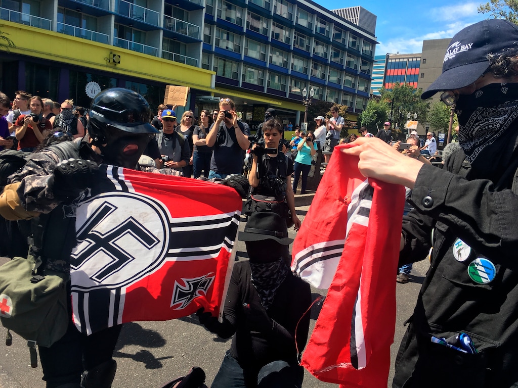 Counter protesters tear a Nazi flag, Saturday, Aug. 4, 2018 in Portland, Ore. Small scuffles broke out Saturday as police in Portland, Oregon, deployed "flash bang" devices and other means to disperse hundreds of right-wing and self-described anti-fascist protesters. (AP Photo/Manuel Valdes)