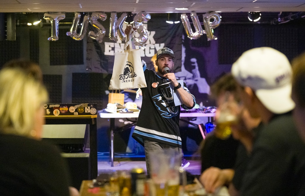 (Bethany Baker  |  The Salt Lake Tribune) Host Austin Facer holds up a raffle prize during a SLC Puck watch party at A Bar Named Sue in Millcreek on Monday, March 16, 2026.