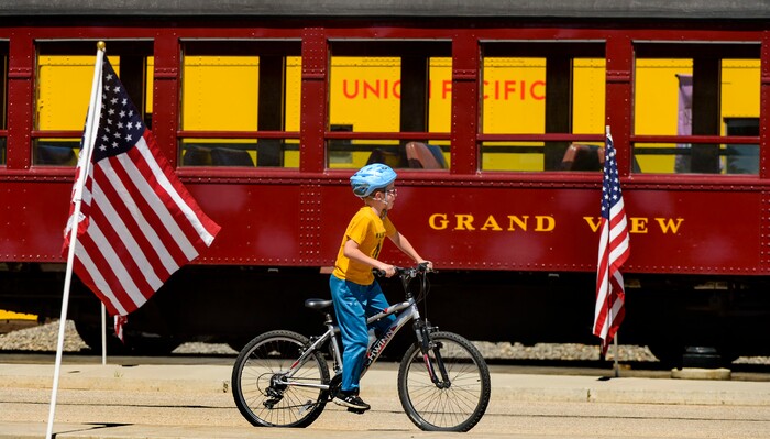 (Leah Hogsten  |  The Salt Lake Tribune) A boy rides past a train car at the historic Heber Valley Railroad as American flags wave in the wind to honor military, past and present, men and women who serve or have served in our Armed Forces in celebration of Heber City 2020 Memorial Day Drive By Tribute, May 25, 2020.