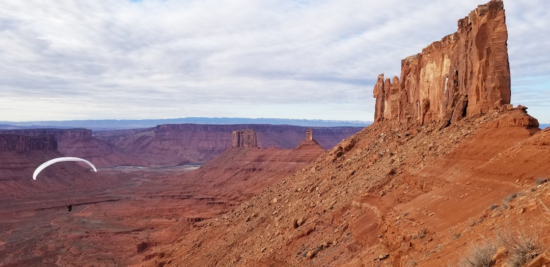 (Kat Vollinger via The New York Times) Nathan Richman paraglides from the base of Castleton Tower, right, after delivering a seismometer to the formation’s summit, in Castle Valley, Utah, March 2018. Castleton Tower taps into the earth’s natural vibrations, and pulsates at about the rate of a human heartbeat.