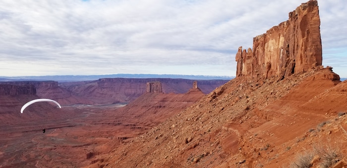 (Kat Vollinger via The New York Times) Nathan Richman paraglides from the base of Castleton Tower, right, after delivering a seismometer to the formation’s summit, in Castle Valley, Utah, March 2018. Castleton Tower taps into the earth’s natural vibrations, and pulsates at about the rate of a human heartbeat.