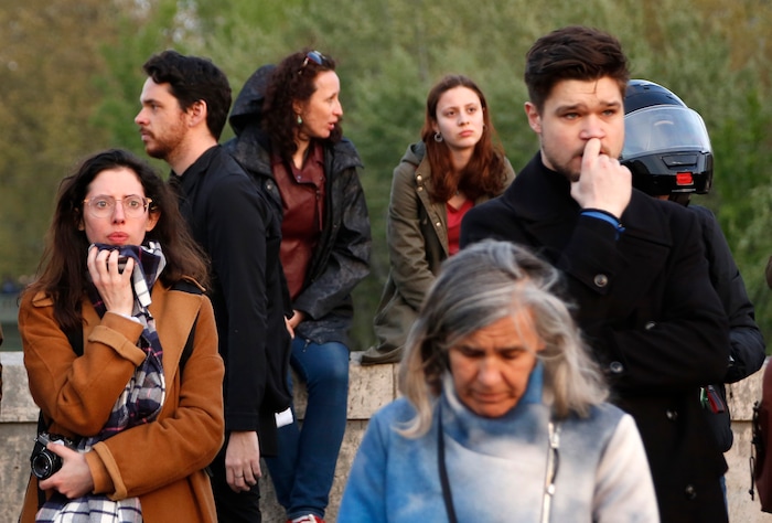 People watch as flames and smoke rise from Notre Dame cathedral as it burns in Paris, Monday, April 15, 2019. Massive plumes of yellow brown smoke is filling the air above Notre Dame Cathedral and ash is falling on tourists and others around the island that marks the center of Paris. (AP Photo/Thibault Camus)