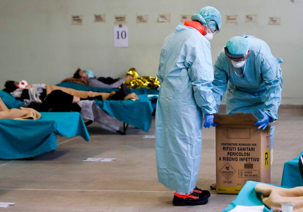 (Luca Bruno | AP) Paramedics carry a hazardous medical waste box as patients lie on camping beds, in one of the emergency structures that were set up to ease procedures at the Brescia hospital, northern Italy, Thursday, March 12, 2020. Italians woke up to yet further virus-containment restrictions after Premier Giuseppe Conte ordered restaurants, cafes and retail shops closed after imposing a nationwide lockdown on personal movement. For most people, the new coronavirus causes only mild or moderate symptoms, such as fever and cough. For some, especially older adults and people with existing health problems, it can cause more severe illness, including pneumonia.
