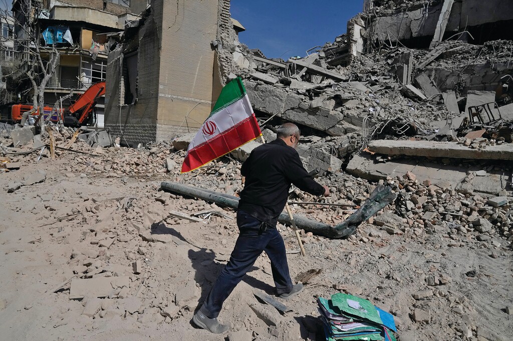 A man carries an Iranian flag to place on the rubble of a police facility struck during the U.S.–Israeli military campaign in Tehran, Iran, Wednesday, March 4, 2026. (AP Photo/Vahid Salemi)