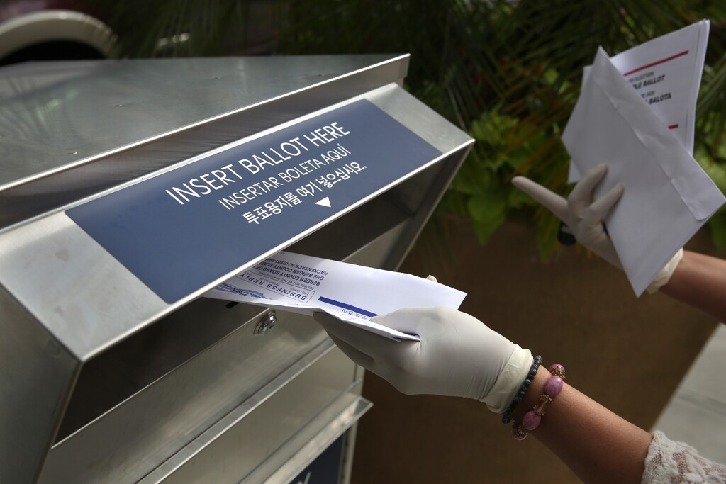 (Seth Wenig | AP file photo)  In this July 7 photo, a woman wearing gloves drops off a mail-in ballot at a drop box in Hackensack, N.J. After months of hearing President Donald Trump denigrate mail-in balloting, Republicans in the critical battleground state now find themselves far behind Democrats in the perennial push to urge their voters to vote remotely. While Democrats have doubled the number of their voters who've asked for a mail ballot compared to 2016, Republicans have only increased by about 20% since the same time.