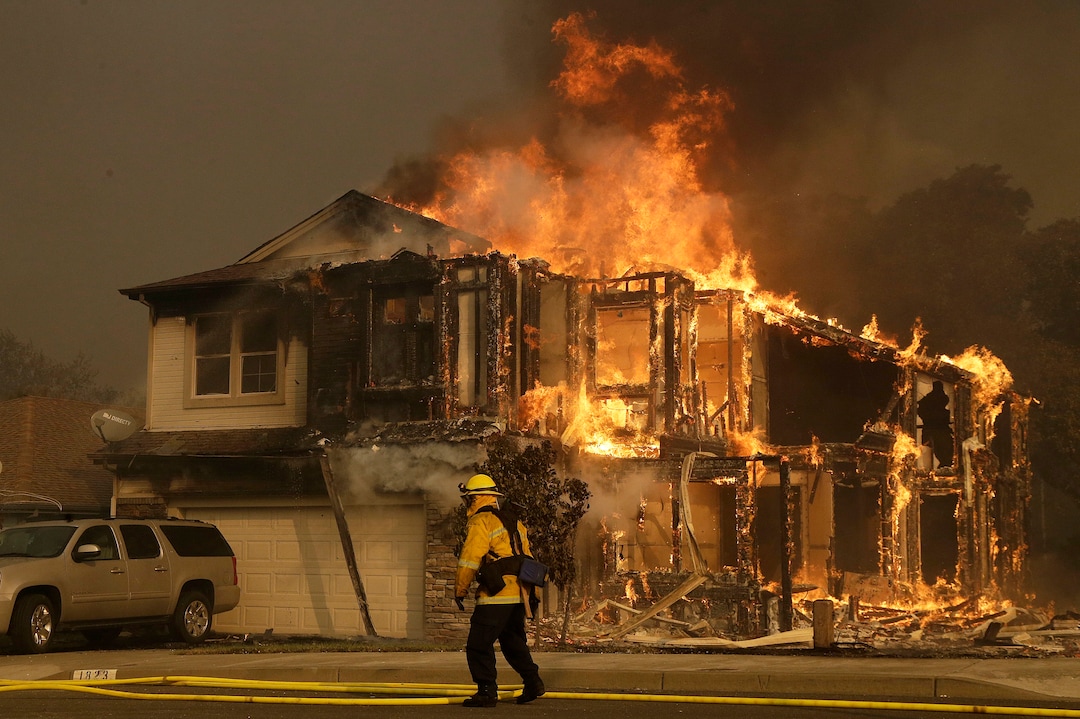 A firefighters walks near a home in Santa Rosa, Calif., Monday, Oct. 9, 2017. Wildfires whipped by powerful winds swept through Northern California sending residents on a headlong flight to safety through smoke and flames as homes burned. (AP Photo/Jeff Chiu)