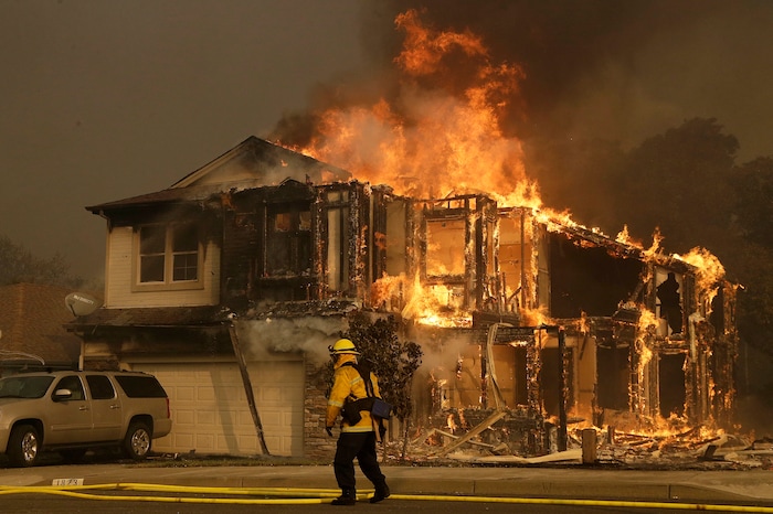 A firefighters walks near a home in Santa Rosa, Calif., Monday, Oct. 9, 2017. Wildfires whipped by powerful winds swept through Northern California sending residents on a headlong flight to safety through smoke and flames as homes burned. (AP Photo/Jeff Chiu)