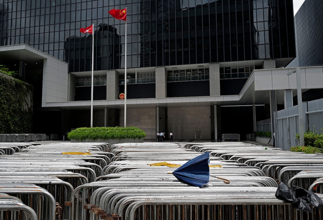 (Vincent Yu | AP Photo) A broken umbrella is seen on barriers against a Hong Kong flag and a Chinese national flag at government headquarters in Hong Kong, Tuesday, July 2, 2019. Hundreds of protesters swarmed into Hong Kong's legislature Monday night, defacing portraits of lawmakers and spray-painting pro-democracy slogans in the chamber before vacating it as riot police cleared surrounding streets with tear gas and then moved inside.