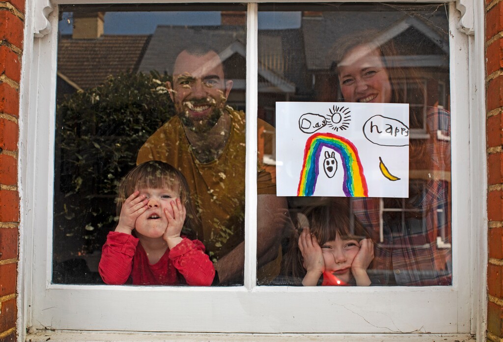 Amelie and her sister, Camille, look out from their front window as the COVID-19 coronavirus lockdown enters it's third week along with their parents, Victoria and Damian Kerr, in Berkhamsted, England, Saturday, April 4, 2020. Victoria and Damian are both working full-time from home, but are enjoying the chance the lockdown has given them to spend more time together as a family despite its challenges. (AP Photo/Elizabeth Dalziel)