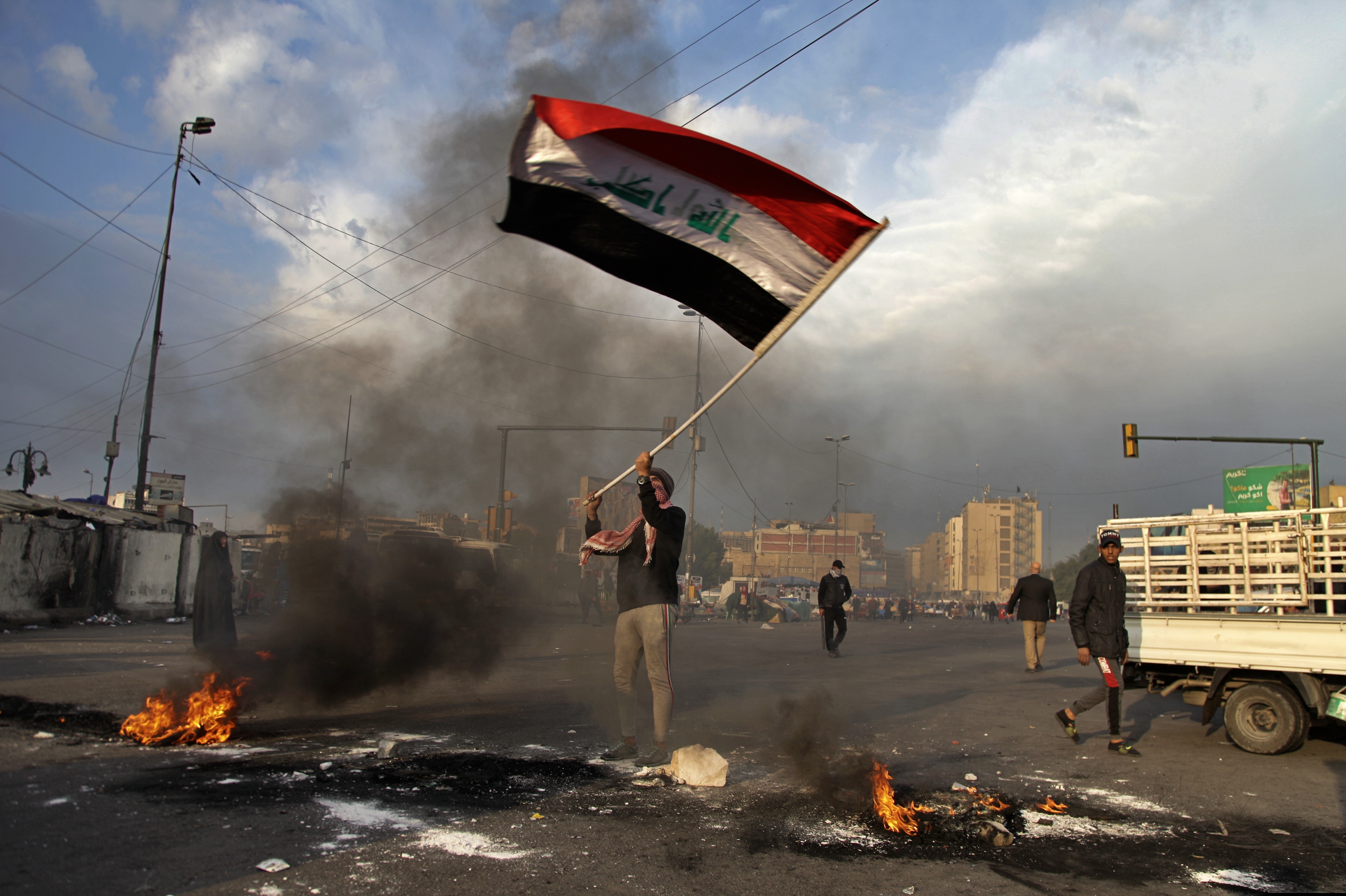 (Khalid Mohammed | AP) A protester waves the national flag while demonstrators set fire to close streets near Tahrir Square during a demonstration against the Iranian missile strike in Baghdad, Iraq, Wednesday, Jan. 8, 2020. Iran struck back at the United States early Wednesday for killing a top Revolutionary Guard commander, firing a series of ballistic missiles at two military bases in Iraq that house American troops in a major escalation between the two longtime foes.