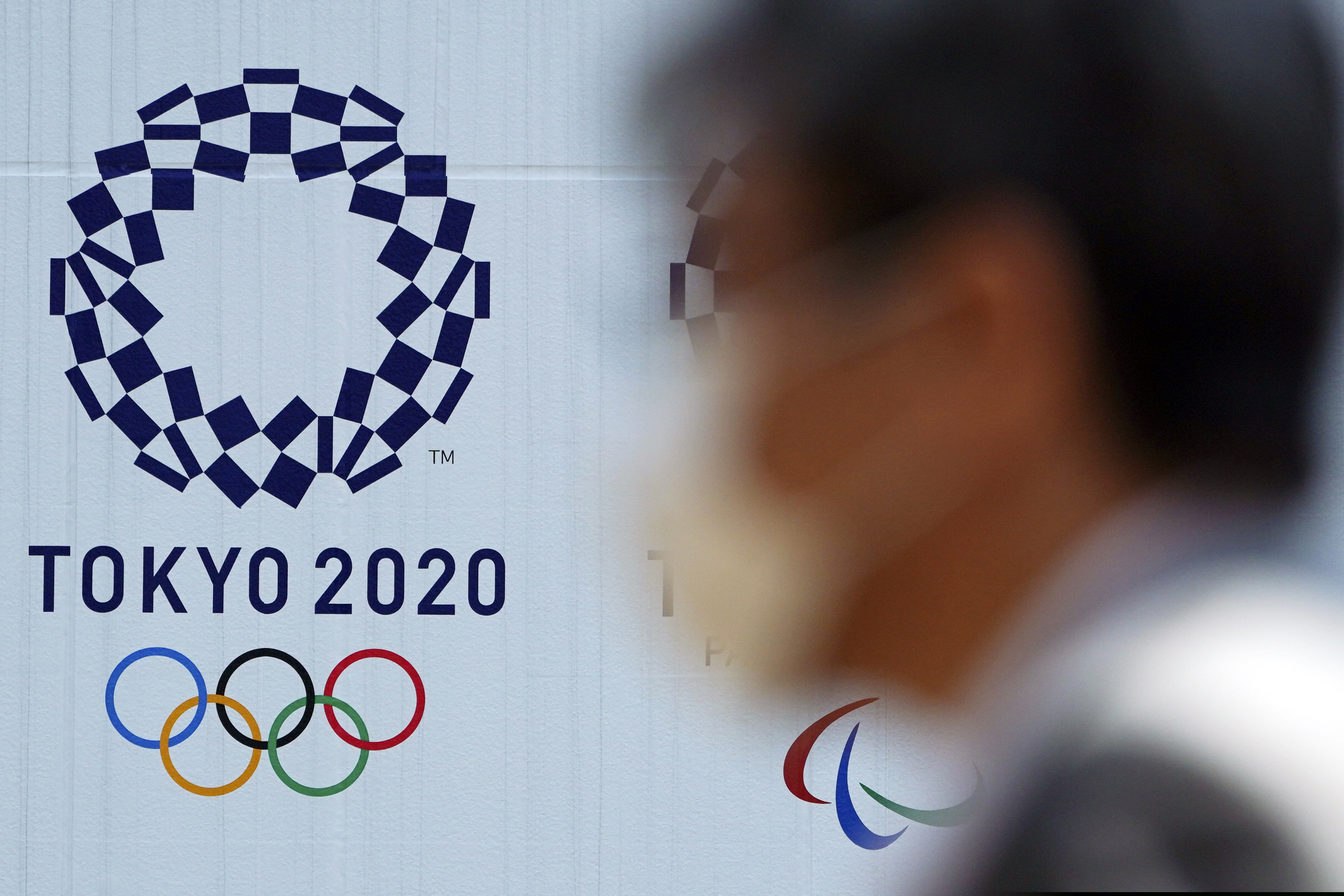 (Eugene Hoshiko | AP) In this April 2, 2020 photo, a man wearing a face mask walks near the logo of the Tokyo 2020 Olympics, in Tokyo. Tokyo organizers said Tuesday, April 14, 2020 they have no “B Plan” for again rescheduling the Olympics, which were postponed until next year by the virus pandemic. They say they are going forward under the assumption the Olympics will open on July 23, 2021.
