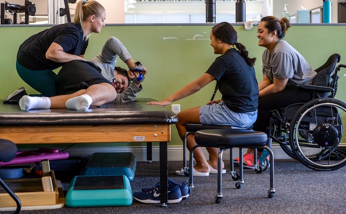 (Leah Hogsten  |  The Salt Lake Tribune) l-r Neuroworx physical therapist Ashlyn Rittmanic works with Stak Afatasi as he works to roll himself into a seated position on his left side under the encouragement of his sisters Amaya, 14, and Justice, 21 on Friday. Audrick “Stak” Afatasi is fighting to regain movement in his lower body after being paralyzed at a trampoline park on March 15, 2019.