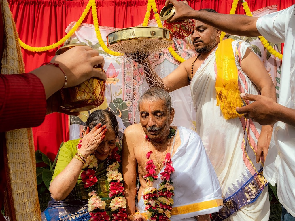 (Bagi Chandrakasan) Family members hold a golden sieve and pour water to drench Indra and Neale Neelameggham during a ceremony on Aug. 24, 2025.