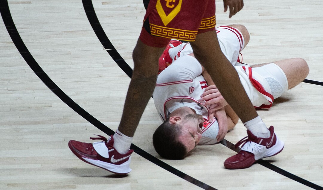 (Francisco Kjolseth  | The Salt Lake Tribune) Utah Utes guard Rylan Jones (15) lies on the floor in pain after colliding with USC Trojans forward Chevez Goodwin (1) in PAC-12 basketball action at the Jon M. Huntsman Center, on Saturday, Feb. 27, 2021.