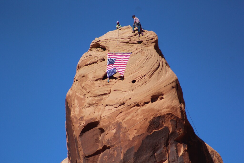 (Doug McMurdo | The Times-Independent) Climbers unfurl an upside down American flag during a protest against the Trump Administration’s mass firing of federal workers, including several in the Moab region, on March 1, 2025.