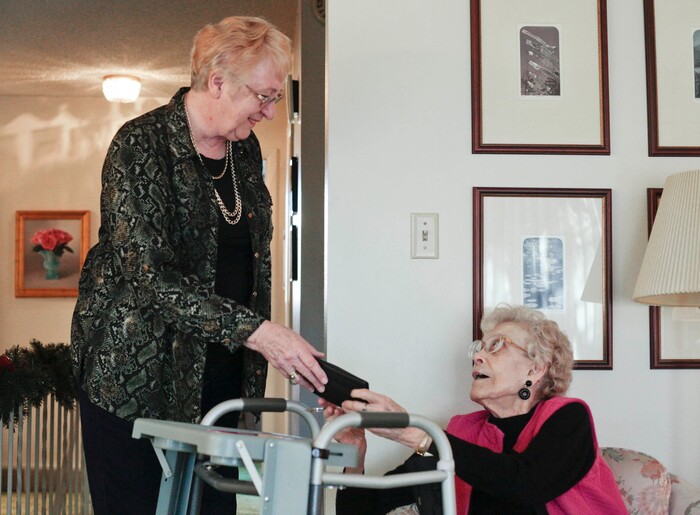 This photo taken Jan. 5, 2018, shows Felicity Varkevisser handing Marian Christensen her wallet in Christensen's house in Provo. Varkevisser volunteers for the Senior Companions program in Utah County and meets with eight individuals each week.  (Evan Cobb/The Daily Herald via AP)