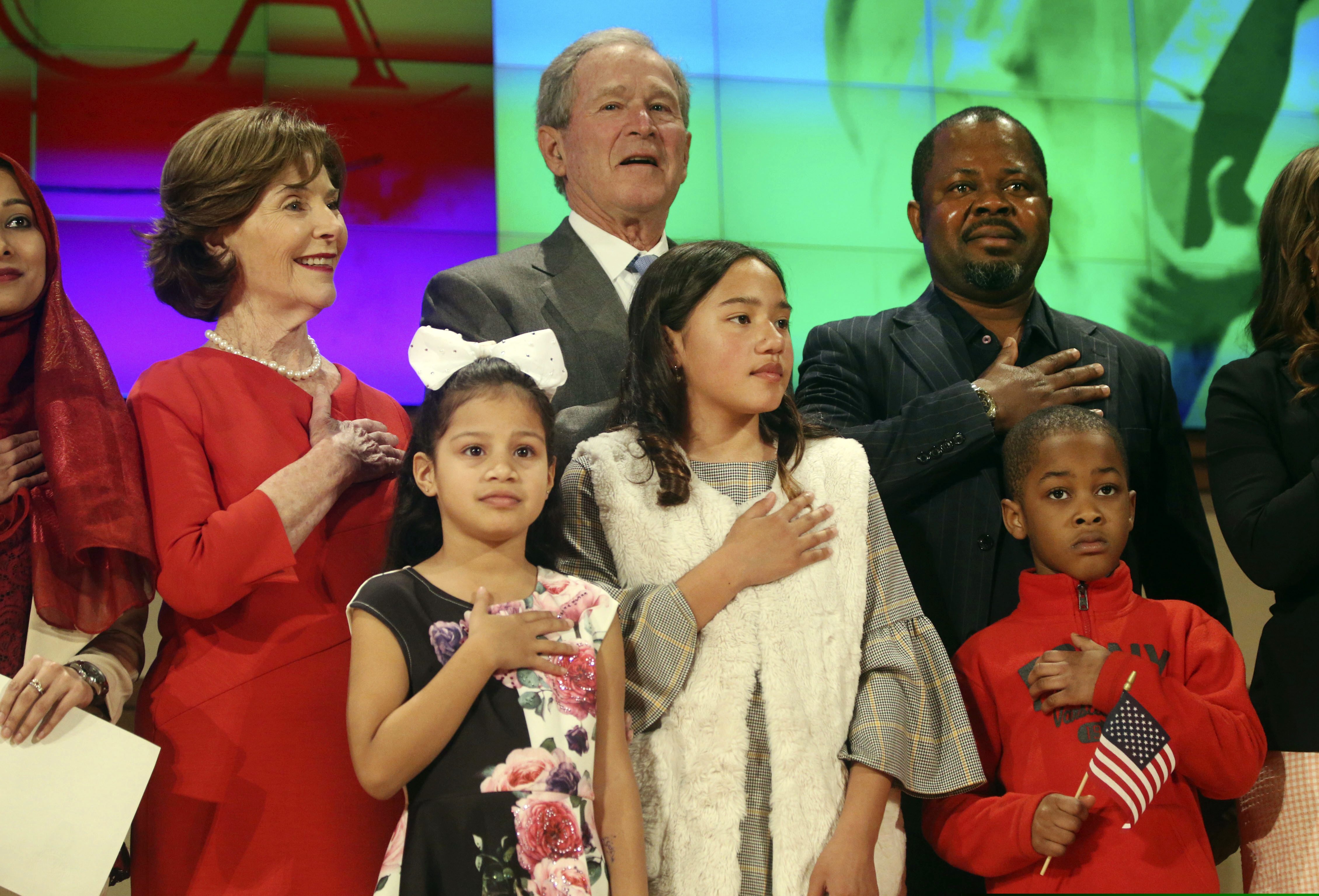 Former President George W. Bush and former first lady Laura Bush recite the pledge of allegiance with new U.S. citizens, including Felix Odeh, (top right) of Nigeria, during a naturalization ceremony at the George W. Bush Presidential Center in Dallas on Monday, March 18, 2019. Forty-nine people representing 20 countries became American citizens at the ceremony. (Rose Baca/The Dallas Morning News via AP)