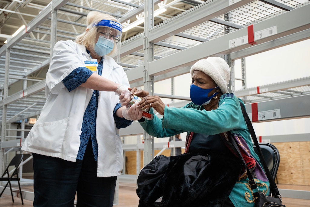 (Pat Nabong/Chicago Sun-Times via AP) Gretchen Leider, a Walmart vision center manager, gives Alice Collins a granola bar while she is under observation after receiving the Moderna COVID-19 vaccine at a Walmart in Chicago, Tuesday, Feb. 2, 2021.