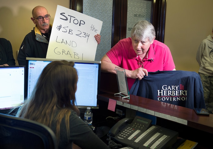 Scott Sommerdorf | The Salt Lake Tribune
Marlene Jennings, right, a former delegate for Gary Herbert when he ran for Governor, came to the Governor's office with others and gave her shirt back over the issue of the inland port and SB234, Thursday, March 14, 2018. Terry Marasco holds a sign indicating the group's hopes that Herbert will not sign SB234 into law, as Jennings hands over her shirt to the Governor's receptionist Brooke Hussey. Herbert was not in the Capitol at the time.