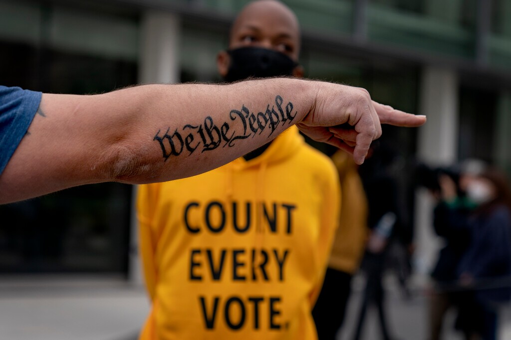In this Nov. 5, 2020, file photo, the tattoo decorates the arm of a Donald Trump supporter as he argues with a counter protestor while Trump supporters demonstrate against the election results outside the central counting board at the TCF Center in Detroit. President Donald Trump and his allies have fomented the idea of a “rigged election” for months, promoting falsehoods through various media and even lawsuits about fraudulent votes and dead voters casting ballots. While the details of these spurious allegations may fade over time, the scar it leaves on American democracy could take years to heal. (AP Photo/David Goldman, File)