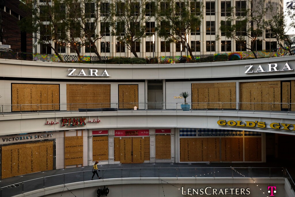 (Jae C. Hong | AP file photo) A woman walks past shops covered in plywood panels to protect the properties against potential vandalism and looting Wednesday, June 3, 2020, in downtown Los Angeles.