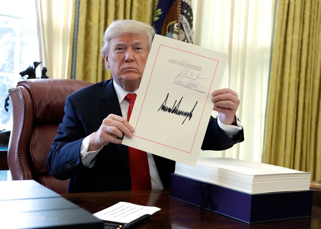President Donald Trump displays the $1.5 trillion tax overhaul package he had just signed, Friday, Dec. 22, 2017, in the Oval Office of the White House in Washington. Trump touted the size of the tax cut, declaring to reporters in the Oval Office before he signed it Friday that "the numbers will speak." (AP Photo/Evan Vucci)