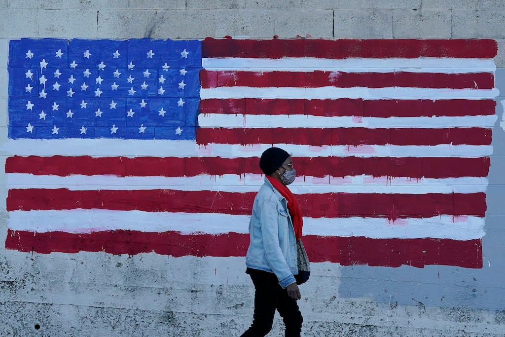 (Jeff Chiu | AP file photo)  A woman wears a mask while walking past an American flag painted on a wall in San Francisco on Nov. 16, 2020.