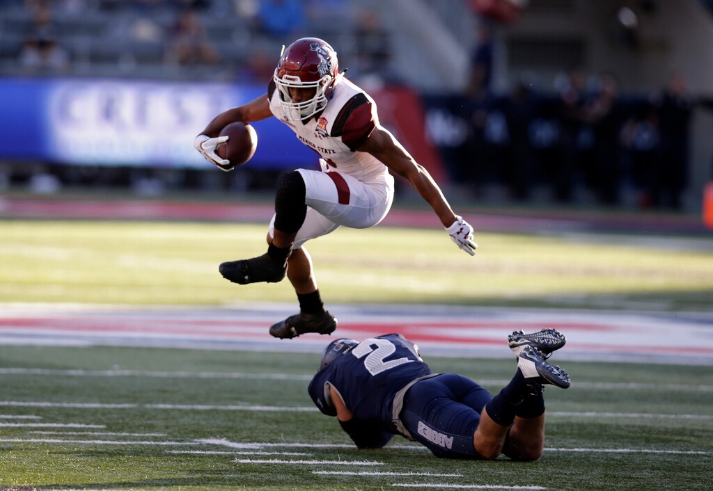 New Mexico State running back Larry Rose III (3) leaps over Utah State safety Dallin Leavitt in the first half during an NCAA college football bowl game, Friday, Dec. 29, 2017, in Tucson, Ariz. (AP Photo/Rick Scuteri)