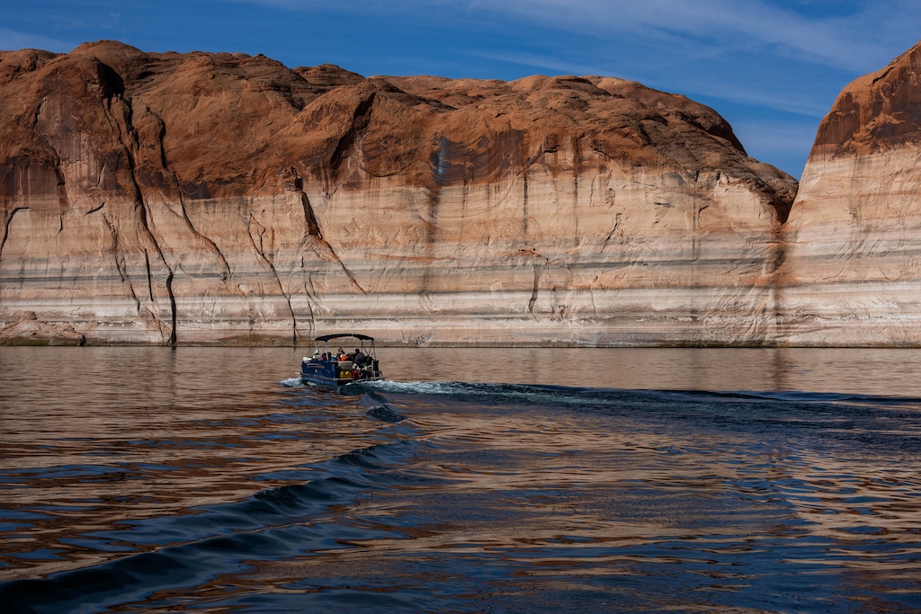 (Francisco Kjolseth | The Salt Lake Tribune) A Lake Powell rental pontoon boat motors down the main channel of the reservoir on Saturday, April 25, 2026, as bathtub rings are indicative of how far the waters levels have fallen since being at full capacity in the early 1980s.