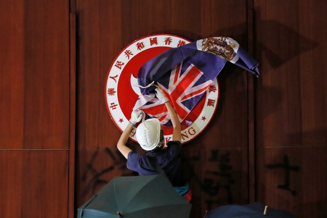 (Kin Cheung | AP Photo) A protester covers the Hong Kong emblem with Hong Kong colonial flag after they broke into the Legislative Council building in Hong Kong, Monday, July 1, 2019.  Protesters in Hong Kong took over the legislature's main building Monday night, tearing down portraits of legislative leaders and spray painting pro-democracy slogans on the walls of the main chamber.