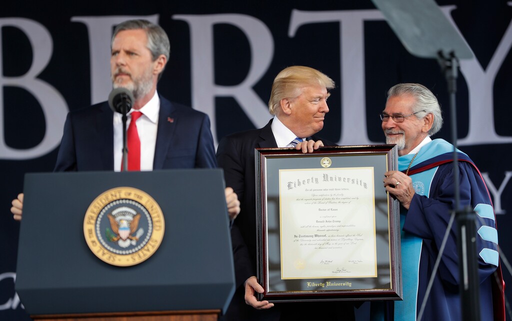 President Donald Trump, center, is presented an Honorary Degree by Ronald E. Hawkins, right, Provost and Chief Academic Officer, before giving the commencement address for the Class of 2017 at Liberty University in Lynchburg, Va., Saturday, May 13, 2017. Speaking at the podium is Liberty University President Jerry Falwell, left. (AP Photo/Pablo Martinez Monsivais)