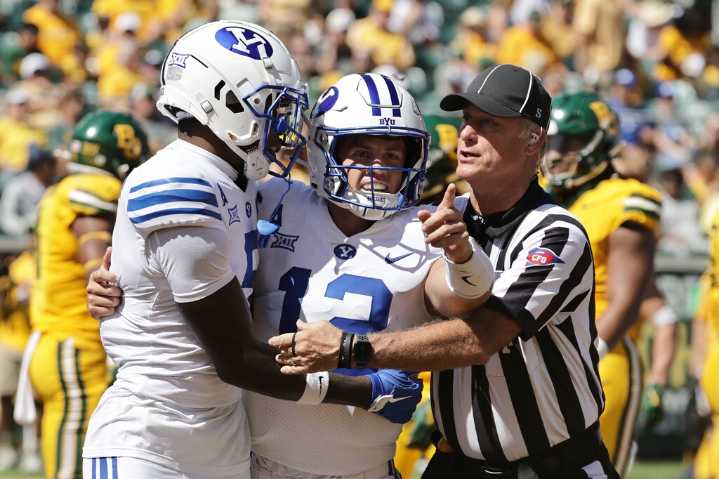BYU quarterback Jake Retzlaff, center, celebrates with wide receiver Darius Lassiter, left, as an official, right, escorts them to the sideline after a touchdown in the first half of an NCAA college football game against Baylor, Saturday, Sept. 28, 2024, in Waco, Texas. (AP Photo/Jerry Larson)