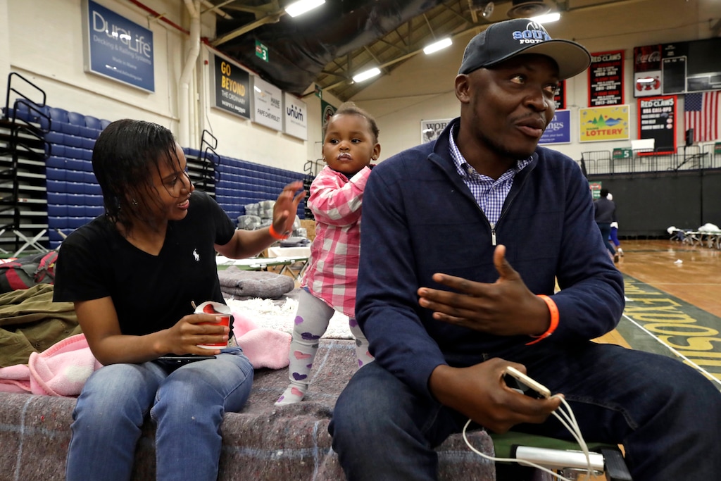 (AP Photo/Elise Amendola) In this June 13, 2019 photo, Prince Pombo speaks about his family's journey as migrants from Africa, at the Portland Exposition Building in Portland, Maine. With him is his wife, Thaiz Neri and their daughter, Heaven. Maine's largest city has repurposed the basketball arena as an emergency shelter in anticipation of hundreds of asylum seekers who are headed to the state from the U.S. southern border. Most are arriving from Congo and Angola.