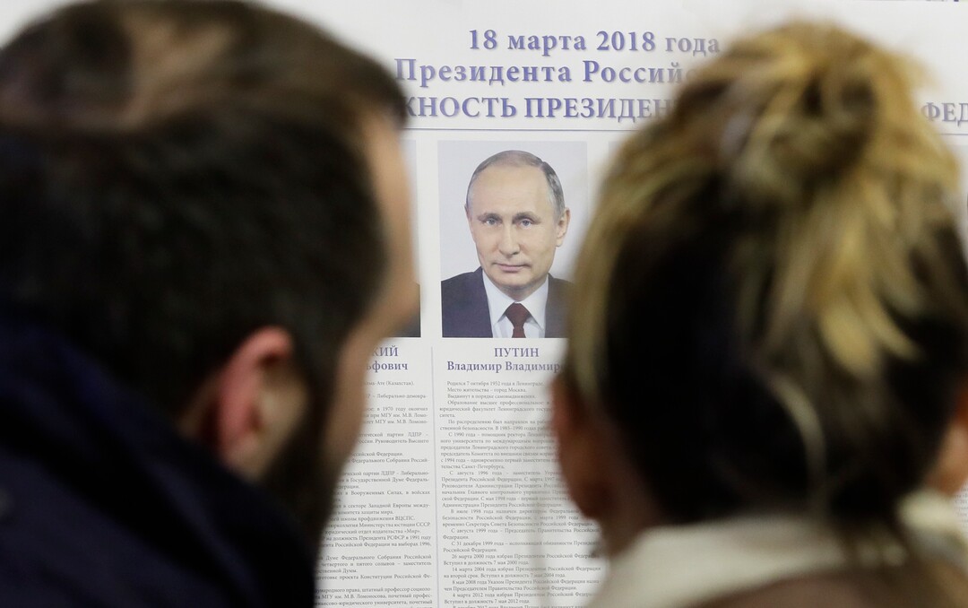 People look at a poster of candidates inside a polling station during presidential elections in St.Petersburg, Russia, Sunday, March 18, 2018. Russians are voting in a presidential election in which Vladimir Putin is seeking a fourth term in the Kremlin. (AP Photo/Dmitri Lovetsky)