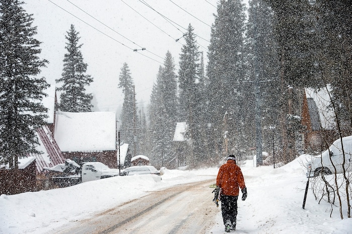 (Chris Detrick | The Salt Lake Tribune) A snowboarder walks along South Brighton Loop Road in Brighton Saturday, December 23, 2017.