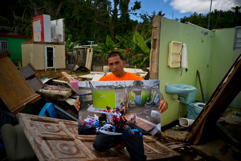 (Ramon Espinosa | The Associated Press) Arden Dragoni holds a printed photo taken on Oct. 5, 2017, that shows him with his wife Sindy, three children and dog Max, amid the remains of his home that was destroyed by Hurricane Maria, as he stands at the same spot where his home remains in shambles in Toa Baja, Puerto Rico, May 28, 2018. The unemployed construction worker and security guard is separated from his family while his wife and children live in a FEMA-subsidized apartment, and he lives with his father. "The hurricane brought us many calamities, but my lesson was to value my family from my heart," said Dragoni.