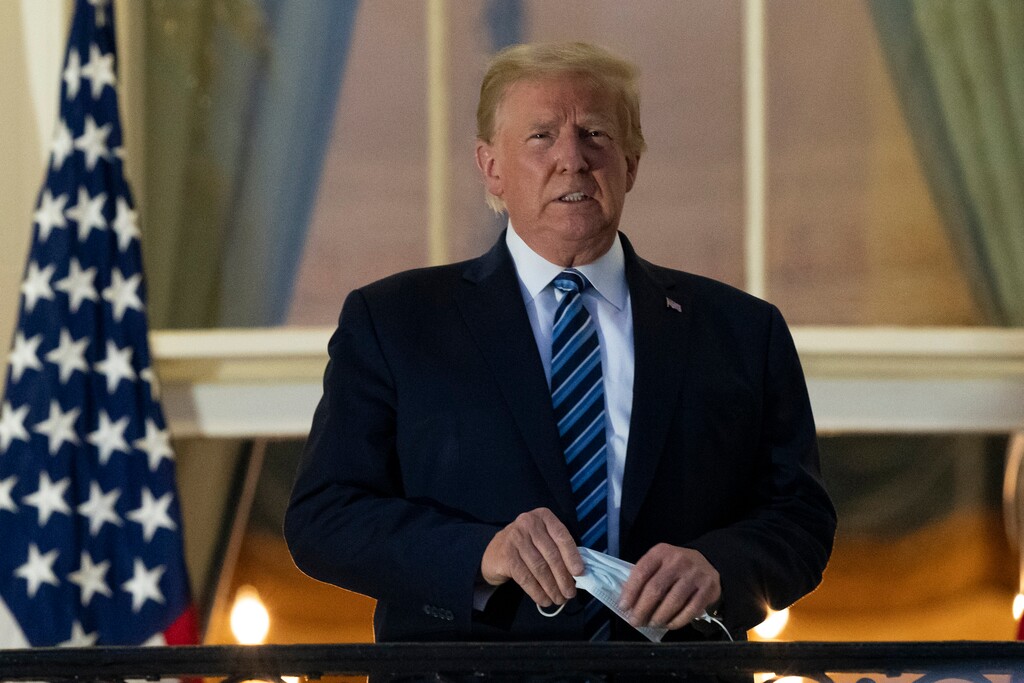 FILE - In this Monday, Oct. 5, 2020 file photo, President Donald Trump removes his mask as he stands on the Blue Room Balcony upon returning to the White House in Washington, after leaving Walter Reed National Military Medical Center, in Bethesda, Md. Trump announced he tested positive for COVID-19 on Oct. 2. (AP Photo/Alex Brandon)