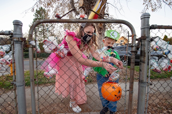 (Francisco Kjolseth  |  The Salt Lake Tribune) Andrea Byron helps her son Leo, 5, pull treat bags off a fence from a household agreeing to abide by CDC Covid safety standards on Saturday, Oct. 31, 2020 in Sugar House.