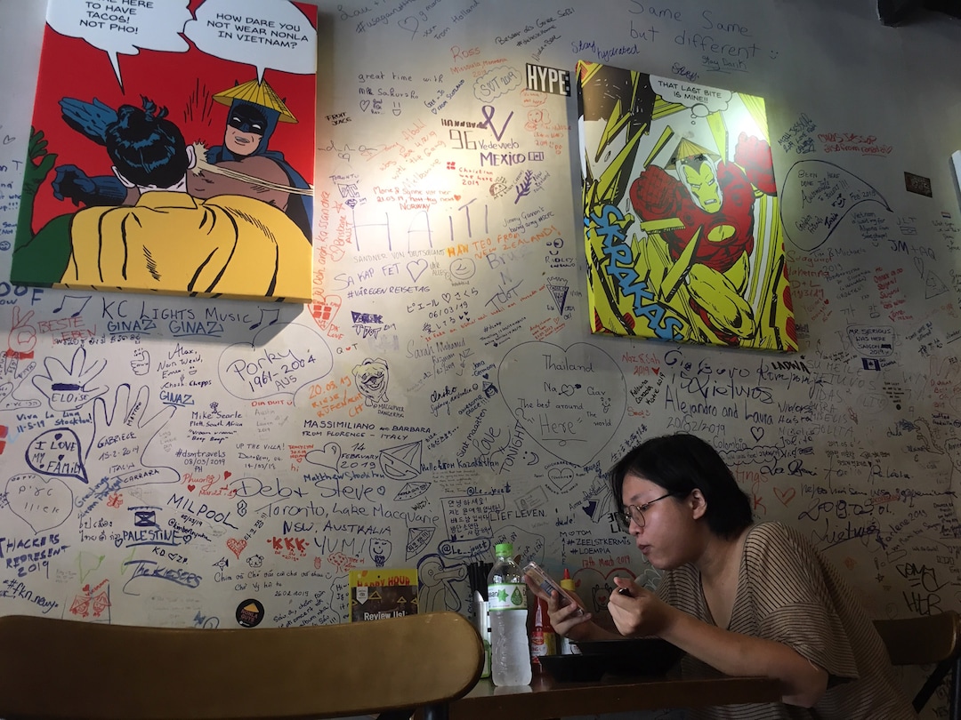 (Matilyn Mortensen | Special to The Tribune) A diner enjoys the Asian-Mexican fusion food of the Nonla Guys restaurant in Ho Chi Mihn City in Vietnam. Superheroes in the artwork are wearing nonlas, traditional woven Vietnamese hats. The restaurant's founders were inspired to start their business by a 2016 documentary on the rebirth of Korean comfort food in the United States, and its segment on the creators of Cupbop in Salt Lake City.