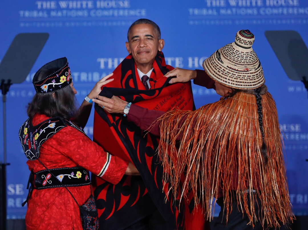Mohegan Chief Lynn Malerba, left, and Brian Cladoosby, right, President of National Congress of American Indians, cover President Barack Obama with a blanket at the 2016 White House Tribal Nations Conference, Monday, Set. 26, 2016, at the Mellon Auditorium in Washington. (AP Photo/Pablo Martinez Monsivais)