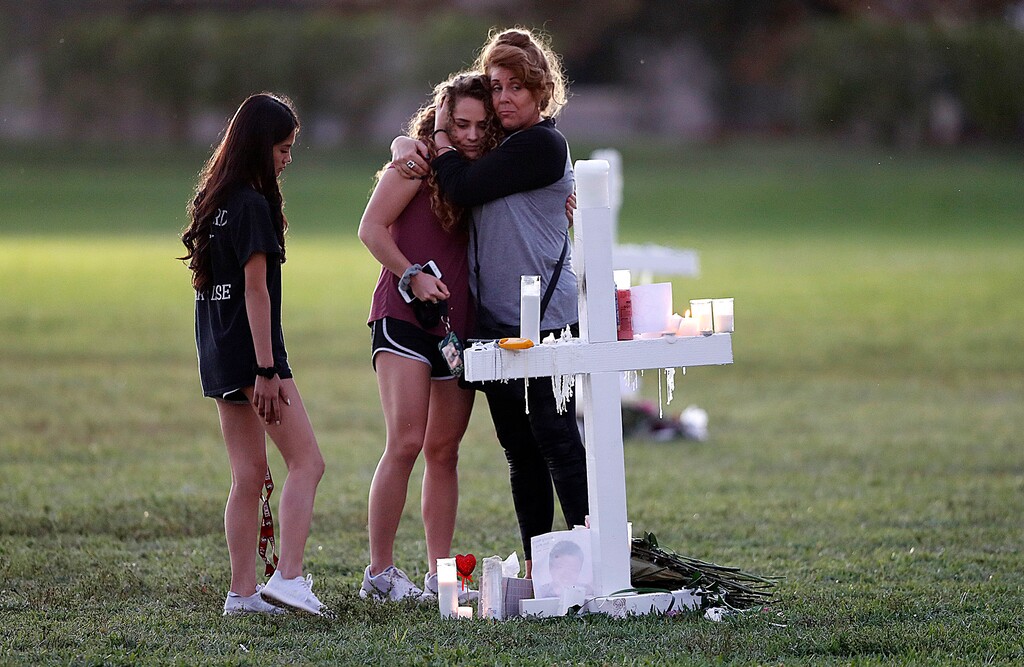 People hug as they pay homage at the memorial crosses, for the 17 deceased students and faculty from the Wednesday shooting at Marjory Stoneman Douglas High School, in Parkland, Fla., Friday, Feb. 16, 2018. Nikolas Cruz, a former student, was charged with 17 counts of premeditated murder on Thursday. (AP Photo/Gerald Herbert)